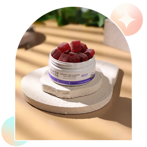 Open jar of Aspen Green USDA Certified Organic Rest CBD Gummies on a stone surface with a blurred outdoor background.