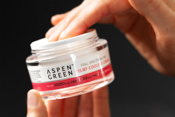 Hand dipping into Aspen Green Relief CBD topical cooling cream jar
