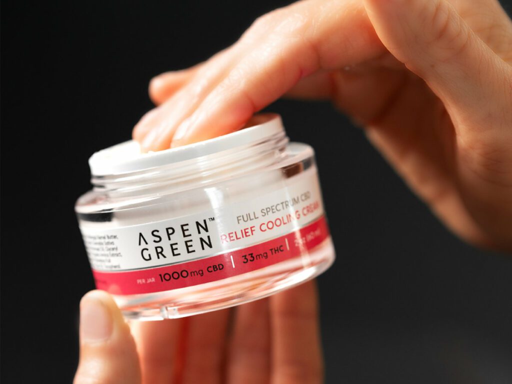 Hand taking Aspen Green Relief Cooling Cream from jar